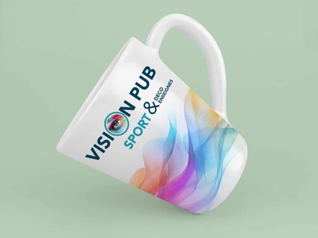 Mug blanc personnalisé pour "VISION PUB", avec un logo d'œil coloré et les textes "SPORT & DECO ENSEIGNES", sur un fond abstrait multicolore.