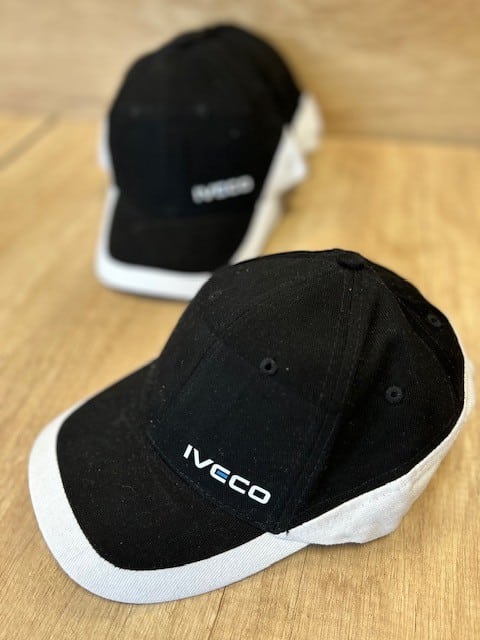 Deux casquettes de baseball Iveco noires avec visière et côtés blancs, posées sur une surface en bois.