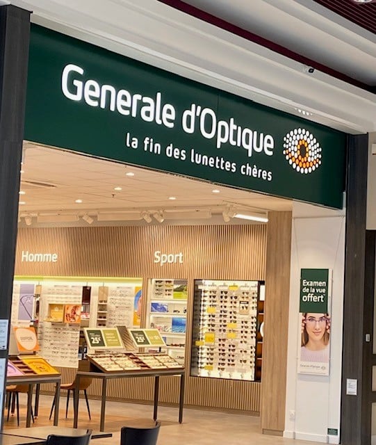 Generale d'Optique : Fin des Lunettes Chères, Examen Offert Enseigne Generale d'Optique "la fin des lunettes chères" avec logo œil. Intérieur lumineux, sections Homme, Sport, et promotion "Examen de la vue offert".